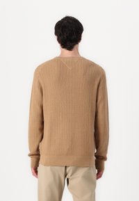 Pull en maille torsadée de couleur fauve, avec un col arrondi et des poignets côtelés. Le motif présente un design en chevrons texturé.