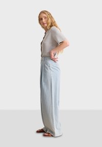 Pantalones de mezclilla de pierna ancha en azul claro, con pliegues frontales y cintura alta, combinados con una blusa gris ajustada de manga corta y textura.