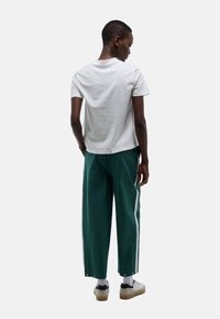 T-shirt blanc à manches courtes associé à un pantalon large vert avec des bandes blanches sur les côtés et des fermetures à pression au niveau de la cheville. Chaussures décontractées incluses.