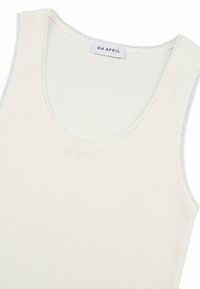 Débardeur blanc côtelé avec bordure en dentelle autour des emmanchures et de l'encolure, avec une étiquette "OH APRIL" au niveau du col arrière.