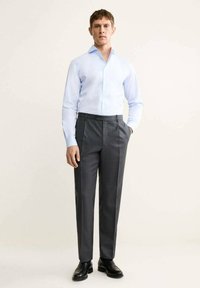 Chemise à manches longues bleu clair associée à un pantalon plissé gris foncé. Le tissu est lisse, avec une coupe ajustée et un design classique. Des chaussures noires complètent le look.