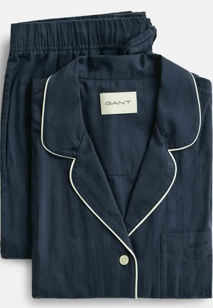 Ensemble de pyjama en coton bleu marine à rayures avec passepoil blanc, comprenant une chemise à col et un pantalon à taille élastique. Étiquette de la marque visible.