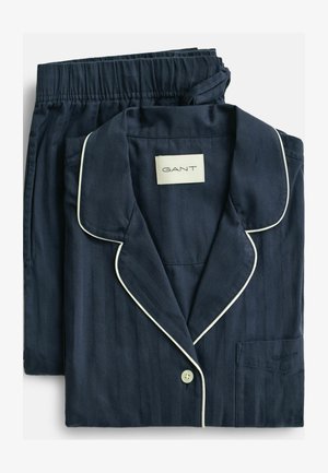 Ensemble de pyjama en coton bleu marine à rayures avec passepoil blanc, comprenant une chemise à col et un pantalon à taille élastique. Étiquette de la marque visible.