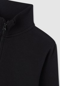 Giacca nera con zip, caratterizzata da un colletto alto, texture a coste e tessuto liscio, che presenta un design minimalista privo di loghi visibili.