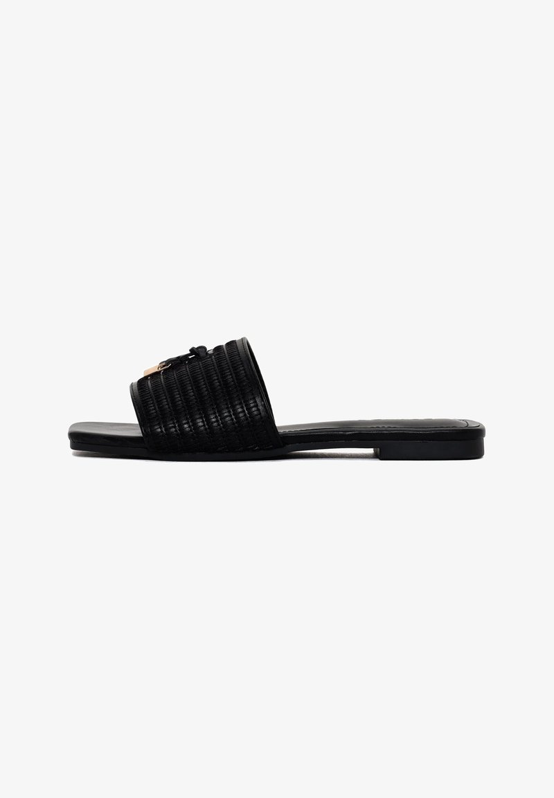 Sandale noire à slide avec un design strié sur le dessus, semelle plate et un petit accent décoratif. Fabriquée en matériau synthétique.