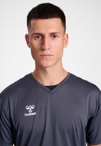 Σκούρο γκρι αθλητικό T-shirt με κοντά μανίκια, σχέδιο V-neck, κατασκευασμένο από λείο, αναπνεύσιμο ύφασμα, με λευκό λογότυπο "hummel" στο στήθος.