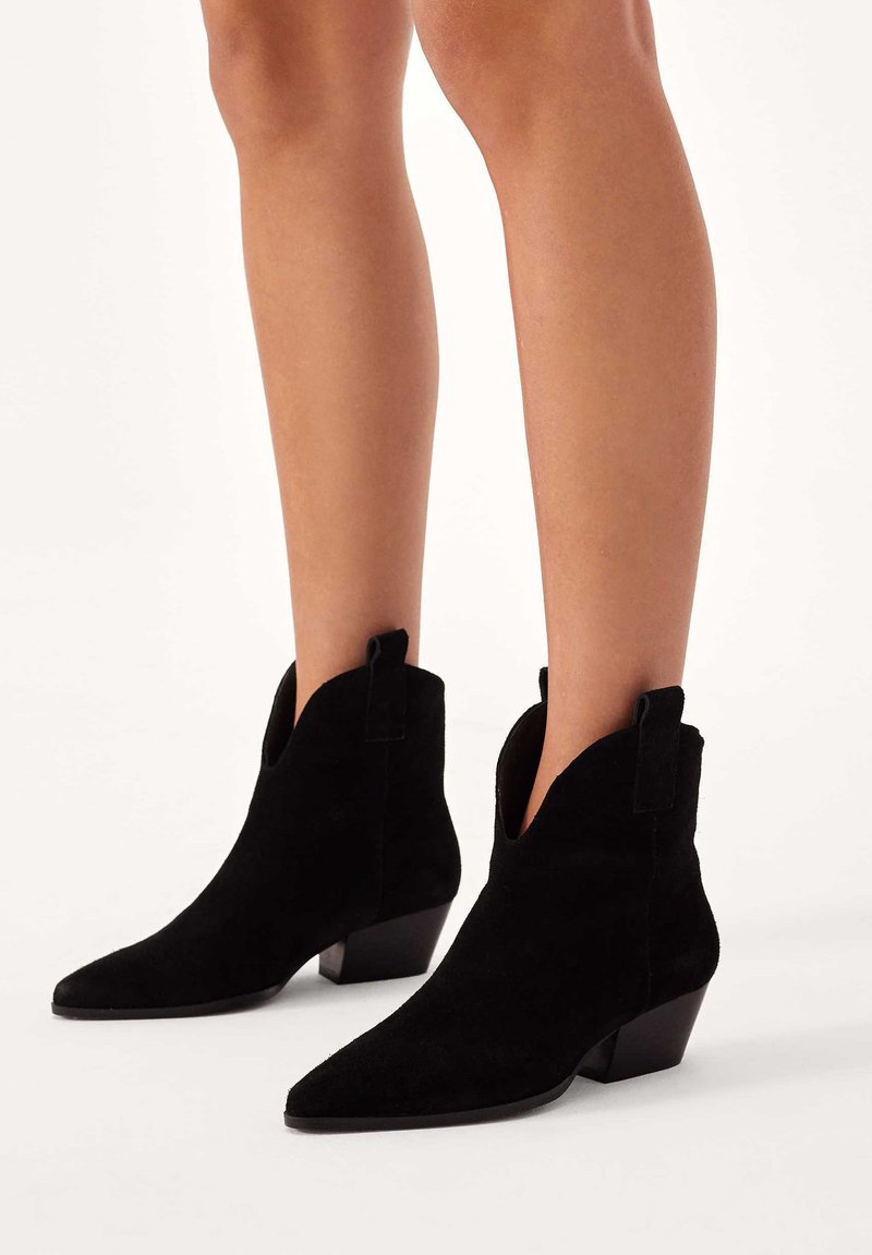 Czarne zamszowe botki za kostkę z wyciągniętym noskiem, niskim blokowym obcasem i wycięciem w kostce. Posiadają pętle ułatwiające zakładanie.