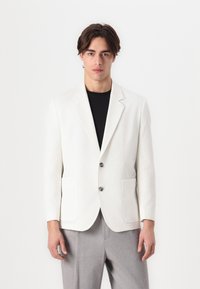 White textured blazer with notched lapels, two front pockets, and buttons, paired with gray trousers. Minimalist design and clean lines.