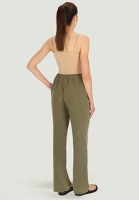 Spodnie oliwkowe z elastyczną talią, wykonane z gładkiego materiału, o luźnym kroju i prostych nogawkach. Połączone z dopasowaną cielistą koszulką na ramiączkach.