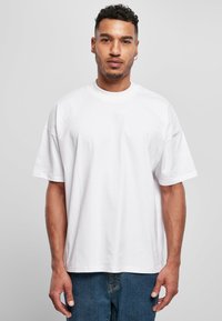 T-shirt bianco in cotone con una vestibilità rilassata, maniche corte, scollatura rotonda e design senza cuciture, indossato con jeans in denim blu.