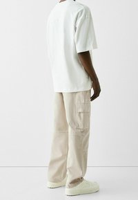 Vit bomullst-shirt i oversize-modell, kombinerad med beige cargo-byxor med flera fickor och en avslappnad passform, fulländad med off-white sneakers.