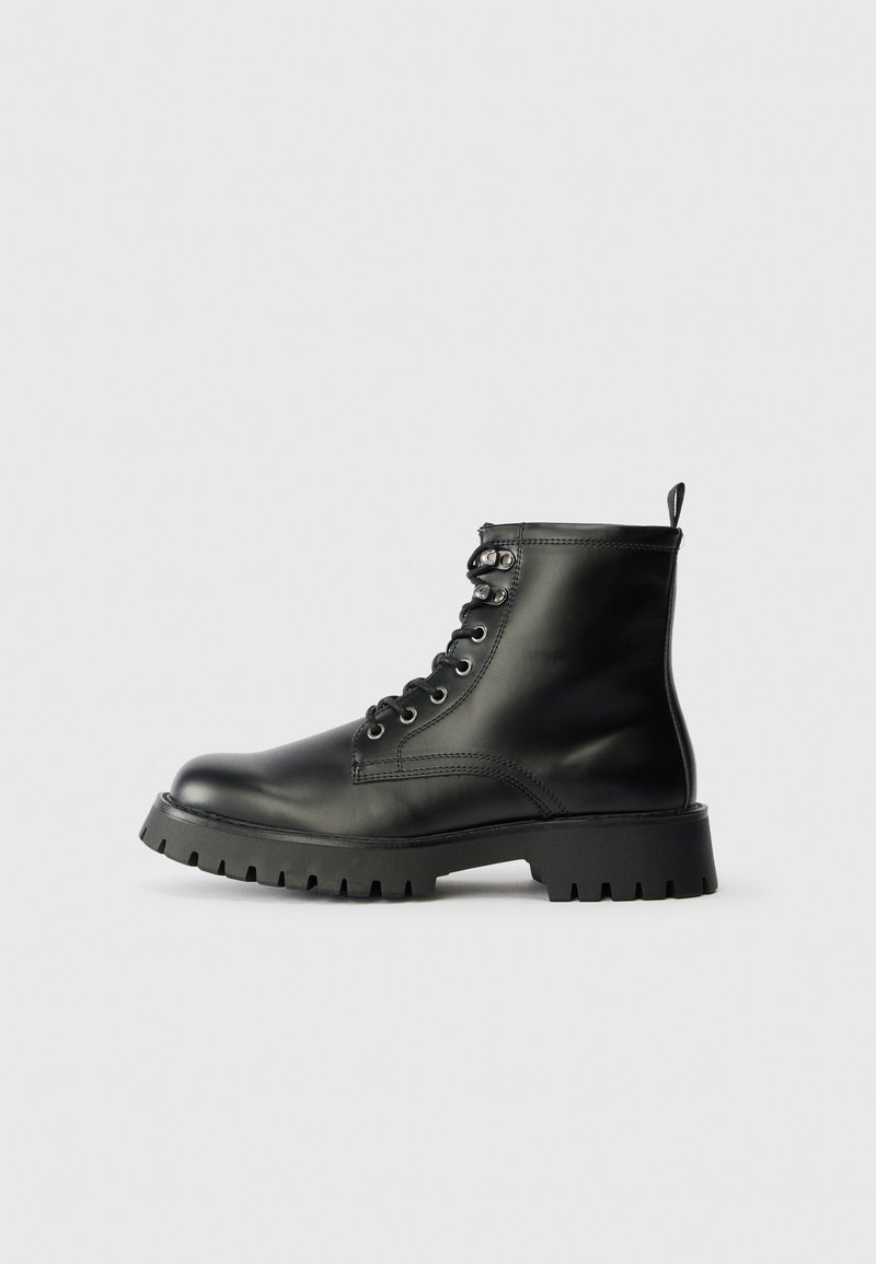Černé kožené kotníkové boty s kulatou špičkou, šesti otvory pro tkaničky a silnou, strukturovanou podrážkou s hlubokými drážkami.
