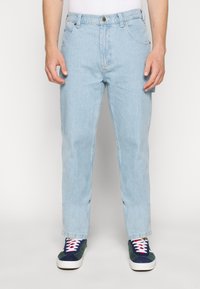Light blue denim pants with a straight fit, five pockets, and a button closure. Worn with multicolored sneakers.