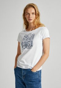 Camiseta de algodón blanca con un diseño gráfico azul con patrones intrincados. La camiseta tiene mangas cortas y un escote redondo.