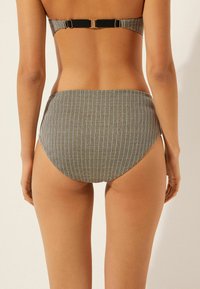 Černobílé pruhované kalhotky od bikin s vysokým pasem, hladkou texturou a širokým pasem. Má minimalistické zlaté kovové detaily.