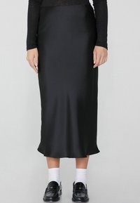 Schwarzer Satin-Midirock mit glatter Textur, Hohe Taille und subtilen Drapierungen. Kombiniert mit schwarzen Schuhen und weißen Socken für einen Kontrast.