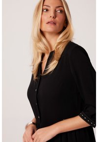 Czarna sukienka z zapięciem na guziki z przodu, długimi rękawami z srebrnymi akcentami oraz plisowaną spódnicą. Gładki materia ł o klasycznym kroju.