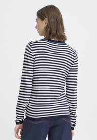 Pull rayé à manches longues en marine et crème, avec un col arrondi et des poignets côtelés. Le tissu semble lisse et ajusté.