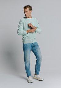 Lichtblauwe sweatshirt met ribgebreide manchetten, gecombineerd met lichtblauwe jeans en witte sneakers. De sweatshirt heeft een ronde hals en een lichte textuur.