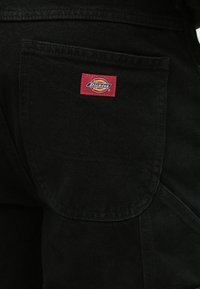 Μαύροί εργασιακοί παντελόνια από τζιν με στρογγυλό κόκκινο και κίτρινο κεντημένο λογότυπο "Dickies" σε τετράγωνο πλακέτα. Διαθέτει πίσω τσέπη με στρογγυλεμένες άκρες.