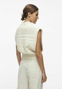 Mouwloze gebreide sweater in crème met ingewikkelde kabelpatronen en een hoge kraag, voorzien van een getextureerde achterkant en een geribbelde zoom.