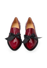 Glanzende rode puntige loafers met zwarte lintstrikken en zwarte zolen, van bovenaf bekeken op een witte achtergrond.