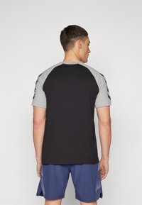 Svart og grå raglan t-skjorte med korte ermer, med en glatt tekstur og kontrastfarge på ermene. Enkelt design uten synlige mønstre.