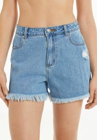 Shorts de mezclilla con un lavado claro, dobladillo deshilachado y detalles desgastados. Presenta una cintura alta y un diseño de cinco bolsillos con herrajes metálicos.