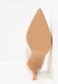 Stiletto en cuir nude avec un bout pointu, texture lisse et une forme élancée et effilée. Semelle antidérapante avec un léger accent à la base du talon.