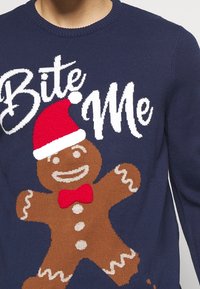 Granatowy sweter z dzianiny z grafiką ludzika z piernika w czerwonym kapeluszu Mikołaja, białym napisem „Bite Me” oraz czerwonymi dodatkami w postaci muszki.