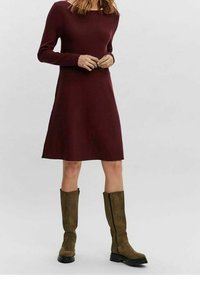 Burgundyröd långärmad klänning med en figursydd överdel och utsvängd kjol. Matchas med knähöga olivgröna stövlar med dragkedja och strukturerad yta.