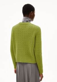 Gebreide trui in een levendig groen met geribde zoom en textuurpatroon. Ronde hals en lange mouwen. Gelaagd gedragen over een grijze top.