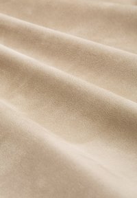 Beżowa tkanina z zamszu o miękkiej, gładkiej fakturze, prezentująca subtelne fałdy i fale, tworzące luksusowy wygląd.