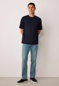 Tengerészkék pamut póló kerek nyakkivágással és rövid ujjakkal, világoskék farmernadrággal és fekete sportcipővel párosítva.