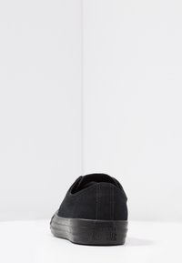 Černé semišové tenisky s nízkým profilem, hladkým povrchem a gumovou podrážkou. Na patě mají branding Converse All Star.