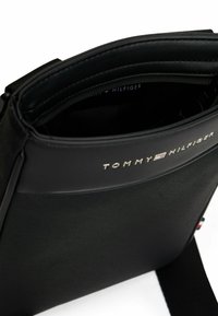 Borsa a spalla nera in tessuto texturizzato, con chiusura superiore con zip, dettagli con logo e tracolla regolabile. Interno foderato in tessuto.