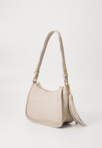 Bolso de hombro de cuero beige con una superficie texturizada, herrajes dorados, cierre de cremallera y un adorno de borla. Cuenta con una correa larga ajustable.