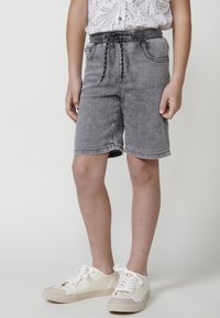 Shorts de denim gris con cintura elástica y cordón, que cuentan con bolsillos frontales y un corte holgado. Llevados con zapatillas blancas.