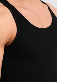 Schwarzes Tanktop aus glattem, dehnbarem Stoff. Hat eine enge Passform, breite Schulterträger und keine sichtbaren Muster oder Metallteile.
