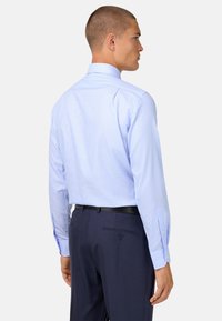 Světle modrá károvaná košile s dlouhými rukávy a špičatým límcem, doplněná o tmavé proužkované kalhoty, pohled zezadu.