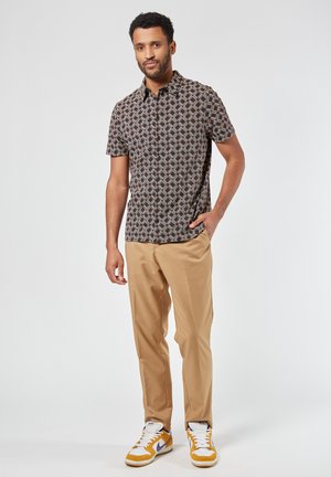 Camicia a maniche corte con motivo in tonalità scure, caratterizzata da forme a diamante in blu e rosso. Abbinata a pantaloni beige e sneaker con dettagli gialli.