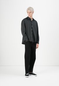 Black and white striped button-up shirt with a loose fit, paired with black pants and black sneakers. Smooth fabric with a slight sheen.