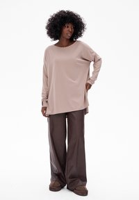 Beige lange mouw top met een ronde hals, gecombineerd met bruine wijde broekspijpen. Zachte textuur met een relaxte pasvorm, zonder zichtbare patronen of accenten.