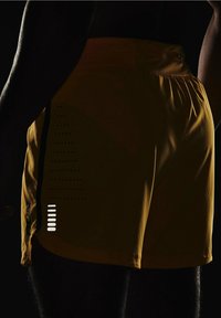 Pantalones cortos deportivos amarillos hechos de tela ligera, con un patrón texturizado y acentos en contraste a los lados.