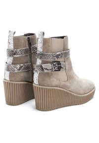 Stivaletti beige in suede con tacco a zeppa rigato. Presentano cinturini con stampa a serpente metallica e chiusura con zip sul retro.