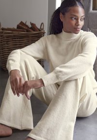 Crème-kleurige, zachte gebreide outfit met een hoge hals trui en wijde broek. Beschikt over ribgebreide manchetten en een relaxte pasvorm voor comfort.