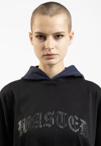 Hanorac oversized negru cu detalii embosate "WASTED"; are o glugă interioară albastră pentru contrast; țesătură moale și texturată.