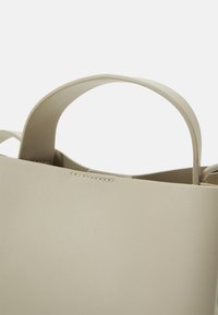 Borsa a mano in pelle beige con manici arrotondati, texture liscia e dettagli di cucitura minimi, che mette in risalto un design geometrico semplice.