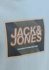 Lichtgrijs T-shirt met een grafische print van "JACK & JONES" in oranje en zwarte letters, inclusief strepen en een randontwerp.