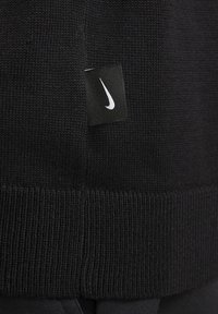 Il tessuto a maglia nera presenta una texture a coste nella parte inferiore, con un piccolo etichetta nera Nike che mostra un logo bianco attaccata.